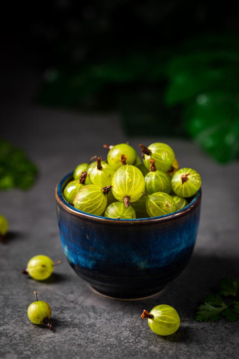 Fresh ripe berries of green gooseberry in a blue bowl on dark gray background. Selective focus.
